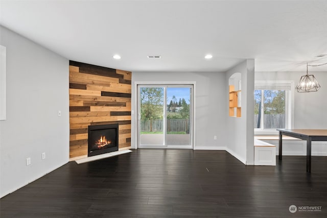 unfurnished living room with a notable chandelier, wooden walls, a fireplace, and dark hardwood / wood-style floors