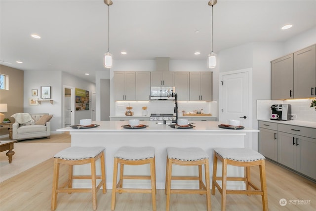 kitchen with gray cabinetry, hanging light fixtures, stainless steel appliances, tasteful backsplash, and a kitchen island with sink