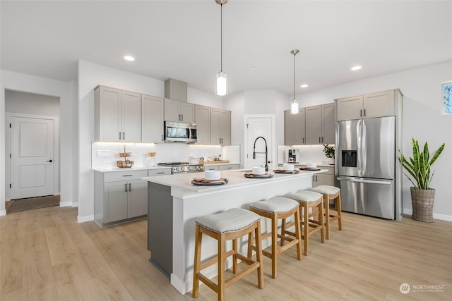 kitchen featuring light wood-type flooring, tasteful backsplash, stainless steel appliances, a kitchen island with sink, and gray cabinets