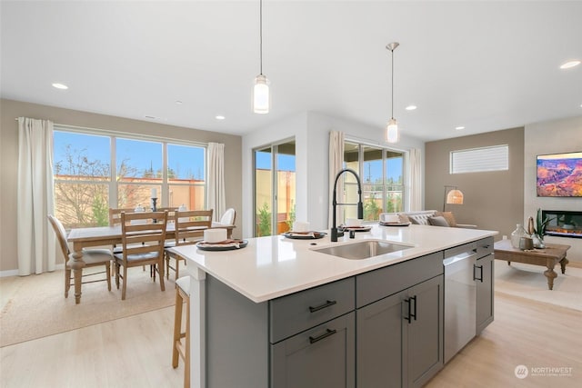 kitchen featuring sink, decorative light fixtures, a center island with sink, dishwasher, and light hardwood / wood-style floors