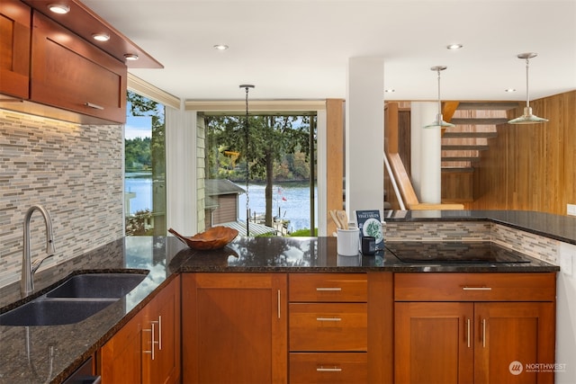 kitchen with dark stone countertops, sink, a water view, and hanging light fixtures