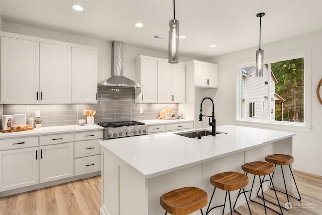 kitchen featuring sink, a center island with sink, and wall chimney range hood