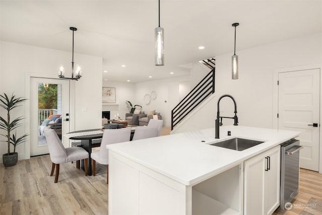 kitchen featuring light wood-type flooring, a kitchen island with sink, sink, pendant lighting, and white cabinetry