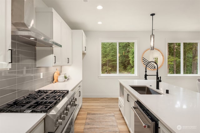 kitchen featuring a wealth of natural light, light wood-type flooring, wall chimney range hood, and appliances with stainless steel finishes