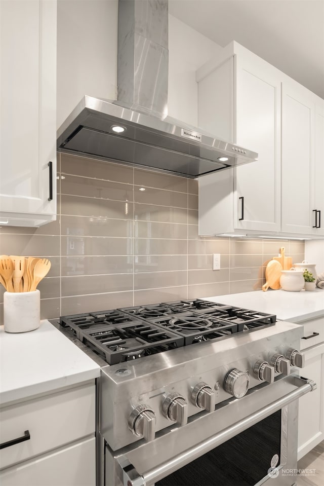 kitchen featuring white cabinets, decorative backsplash, high end stove, and wall chimney exhaust hood