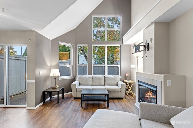 living room featuring a towering ceiling, wood-type flooring, plenty of natural light, and a tile fireplace