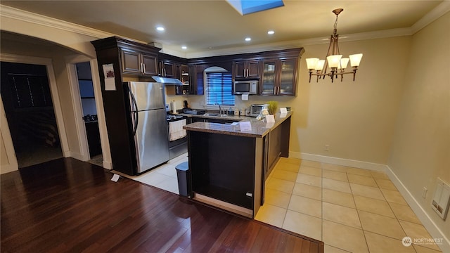 kitchen with kitchen peninsula, dark brown cabinets, stainless steel appliances, light stone countertops, and light tile patterned floors