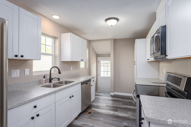 kitchen with appliances with stainless steel finishes, sink, white cabinetry, a wealth of natural light, and dark wood-type flooring