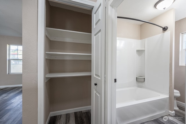 bathroom featuring  shower combination, hardwood / wood-style flooring, and toilet