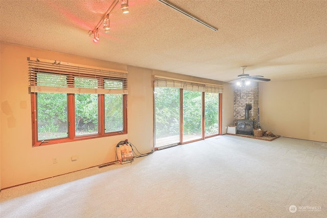 unfurnished living room with a textured ceiling, a wood stove, track lighting, carpet flooring, and ceiling fan