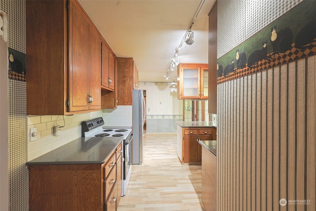 kitchen with electric range oven, decorative backsplash, stainless steel refrigerator, and light hardwood / wood-style flooring