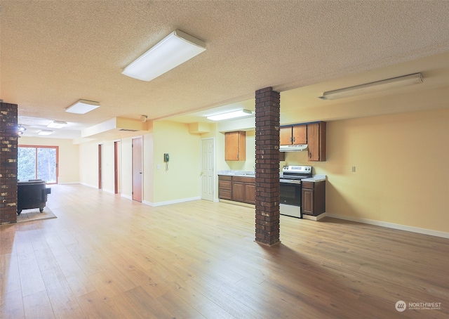 interior space featuring decorative columns, a wood stove, a textured ceiling, and light hardwood / wood-style floors