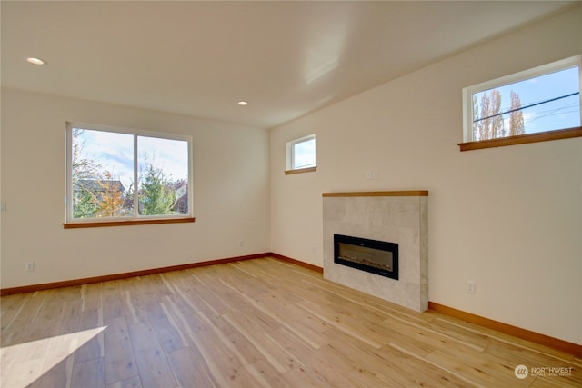 unfurnished living room with a tile fireplace, a healthy amount of sunlight, and light hardwood / wood-style flooring