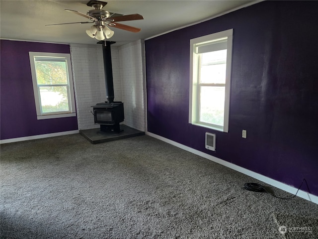 unfurnished living room featuring carpet, ceiling fan, and a wood stove