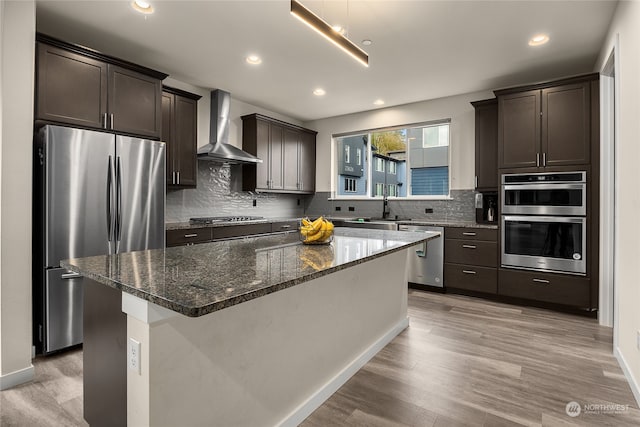 kitchen with wall chimney exhaust hood, a center island, light hardwood / wood-style floors, and stainless steel appliances