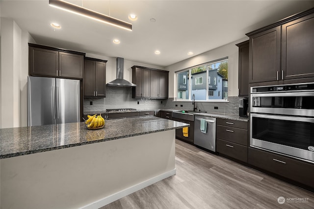 kitchen featuring tasteful backsplash, wall chimney exhaust hood, stainless steel appliances, and light wood-type flooring