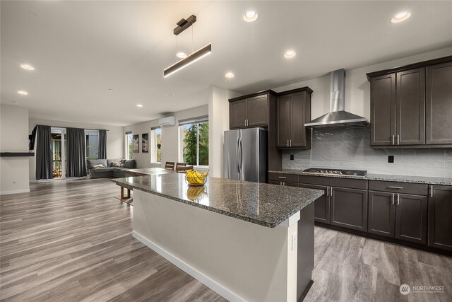 kitchen with wall chimney exhaust hood, stainless steel fridge, gas stovetop, decorative backsplash, and light hardwood / wood-style floors