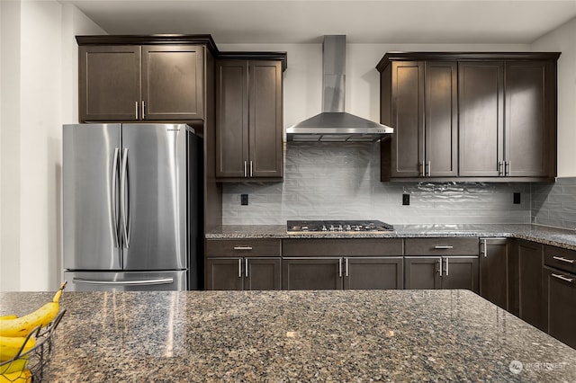 kitchen featuring backsplash, stainless steel appliances, dark stone counters, and wall chimney exhaust hood