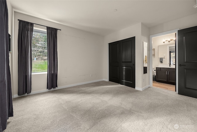 unfurnished bedroom featuring light carpet, connected bathroom, and sink