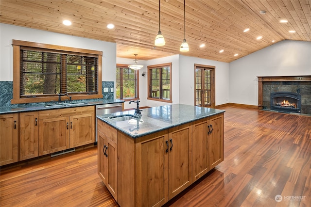 kitchen featuring a center island with sink, hardwood / wood-style flooring, pendant lighting, and dark stone countertops