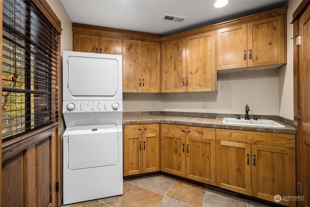 laundry room with sink, stacked washer / dryer, and cabinets