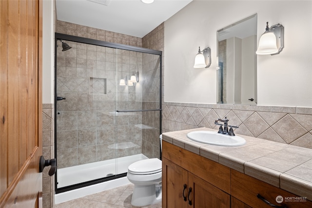 bathroom featuring tile walls, toilet, a shower with shower door, vanity, and tile patterned flooring