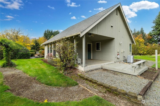 back of house with a lawn, a wooden deck, a patio area, and roof with shingles