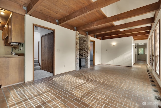 unfurnished living room featuring beamed ceiling, sink, a wood stove, and wooden ceiling