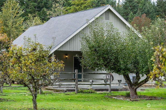 view of front of house featuring covered porch, board and batten siding, roof with shingles, and a front lawn