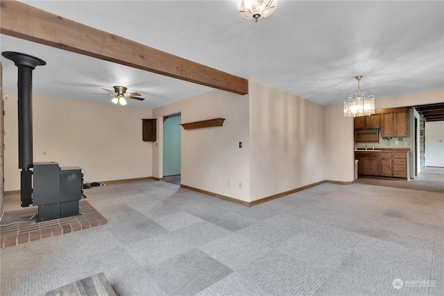 unfurnished living room featuring baseboards, a wood stove, ceiling fan with notable chandelier, and light carpet