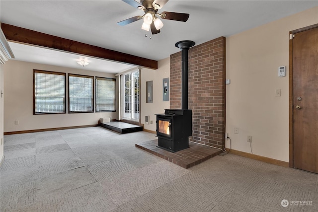 unfurnished living room featuring a wood stove, beam ceiling, baseboards, a ceiling fan, and carpet