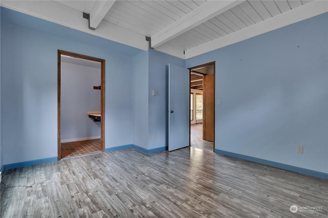 empty room with baseboards, wood finished floors, and beamed ceiling