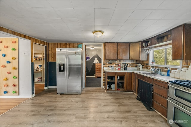 kitchen with light hardwood / wood-style flooring, wood walls, stainless steel appliances, and sink