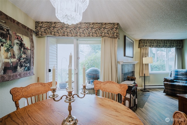 dining area with a notable chandelier, wood-type flooring, a textured ceiling, and a baseboard heating unit