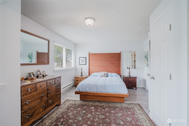 bedroom with a textured ceiling, a baseboard radiator, and light hardwood / wood-style flooring