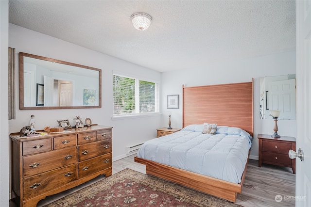 bedroom with light hardwood / wood-style flooring, a textured ceiling, and a baseboard heating unit