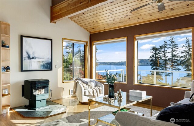 living room featuring vaulted ceiling with beams, light wood-type flooring, a wood stove, wooden ceiling, and a water view