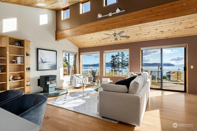 living room featuring light hardwood / wood-style flooring, a wood stove, wooden ceiling, lofted ceiling with beams, and a water view