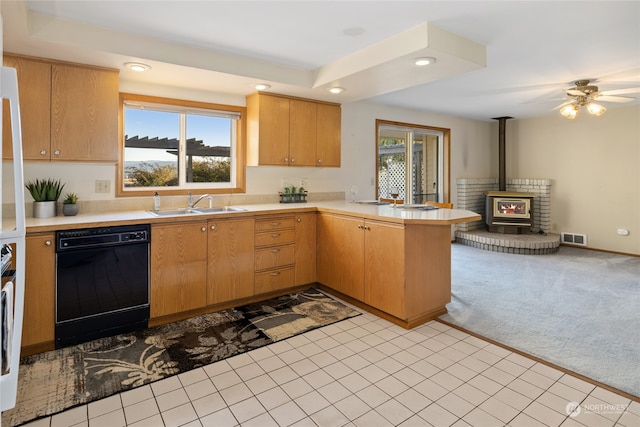 kitchen featuring light colored carpet, a wood stove, kitchen peninsula, black dishwasher, and sink