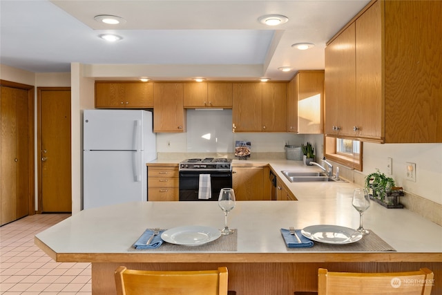 kitchen featuring sink, kitchen peninsula, stainless steel range oven, and white fridge