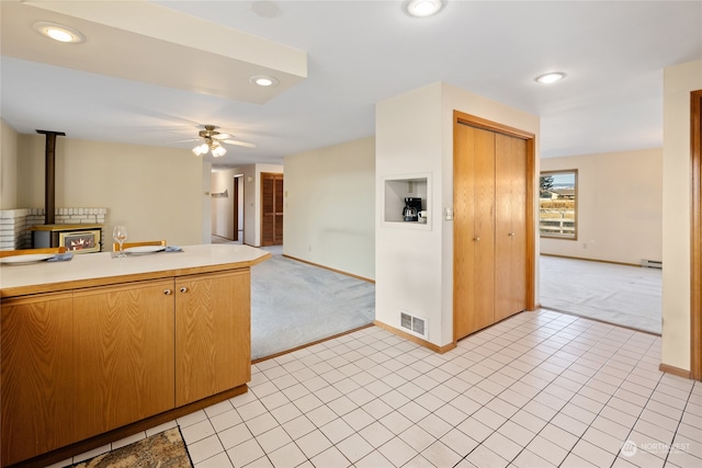 kitchen with ceiling fan, light colored carpet, a wood stove, and baseboard heating