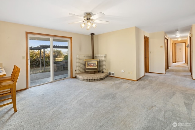 unfurnished living room featuring a wood stove, light carpet, and ceiling fan