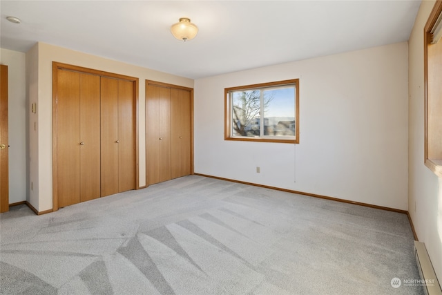 unfurnished bedroom featuring light carpet, baseboard heating, and two closets