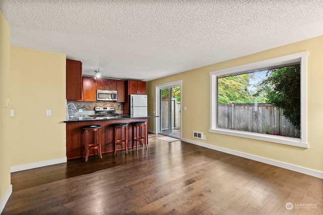 kitchen with dark hardwood / wood-style floors, tasteful backsplash, stainless steel appliances, and a kitchen bar