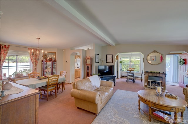 carpeted living room featuring vaulted ceiling with beams, a chandelier, a wealth of natural light, and a tiled fireplace