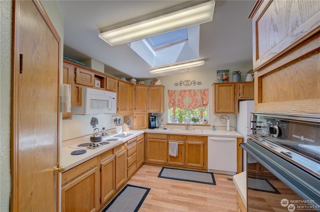 kitchen featuring sink, white appliances, light hardwood / wood-style flooring, and a skylight