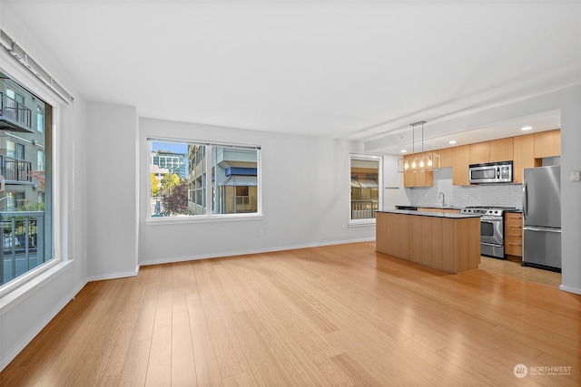 kitchen with a kitchen island, tasteful backsplash, decorative light fixtures, light wood-type flooring, and stainless steel appliances