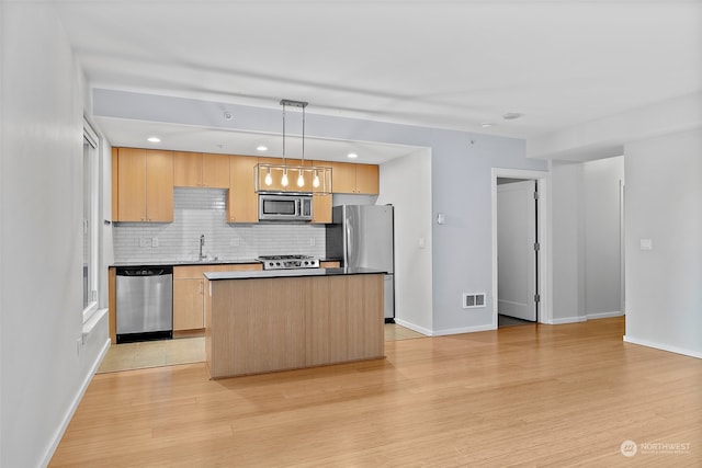 kitchen with light hardwood / wood-style flooring, a kitchen island, appliances with stainless steel finishes, and pendant lighting