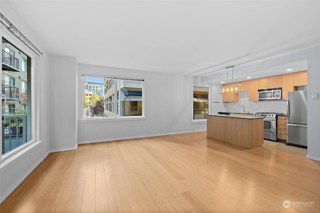 kitchen with decorative backsplash, appliances with stainless steel finishes, pendant lighting, light hardwood / wood-style flooring, and a kitchen island