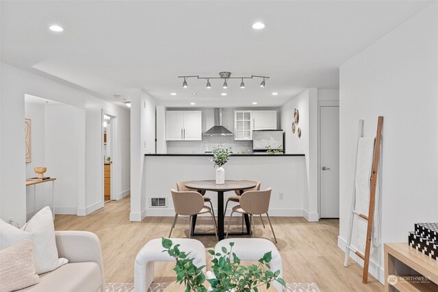 interior space with decorative backsplash, wall chimney exhaust hood, white cabinetry, light hardwood / wood-style floors, and stainless steel refrigerator